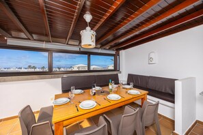 Ein Essbereich mit Holztisch, gedeckt für vier Personen, einer Couch und Blick auf das Meer.