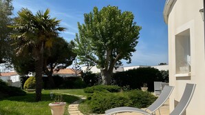 Une terrasse avec des chaises longues, un chemin et un jardin agrémenté d’arbres et d’arbustes.