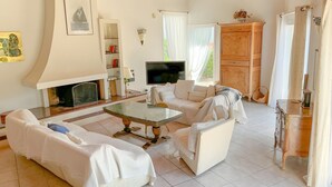 Un salon avec une cheminée, des meubles blancs, un téléviseur et une vue sur l’extérieur.