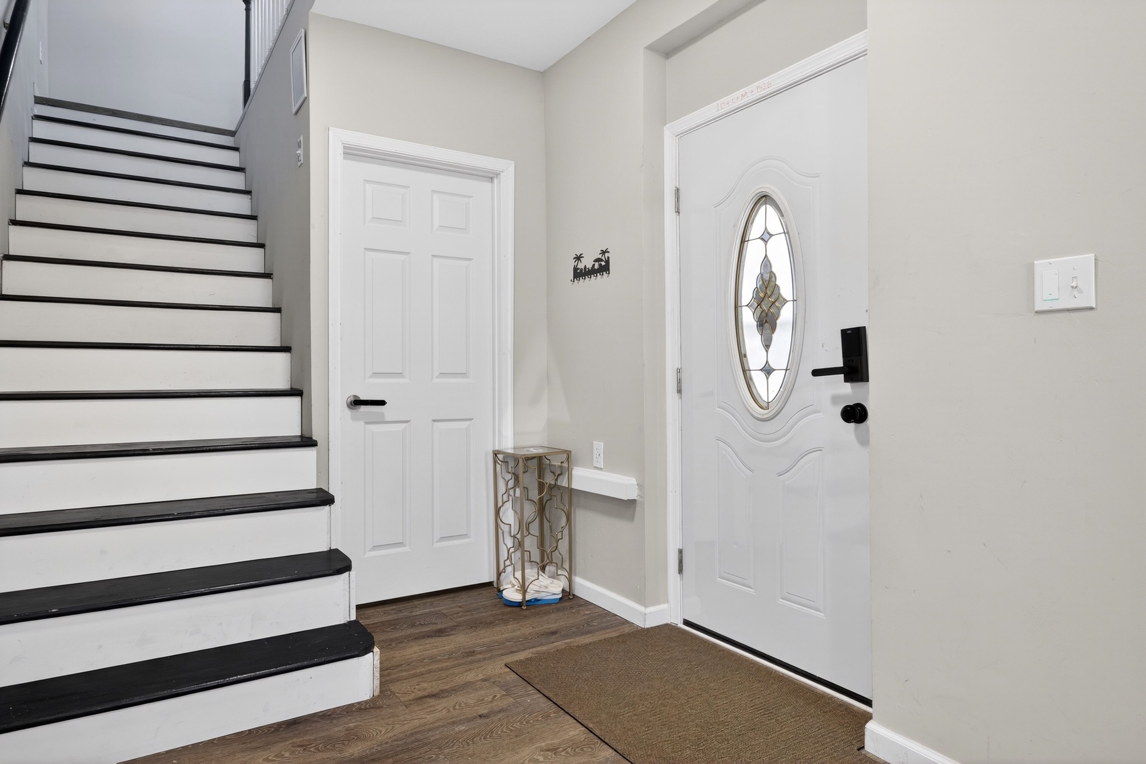 Un escalier menant à une porte ornée d’un panneau de verre décoratif, une petite étagère et une poubelle.