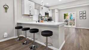 Een moderne keuken met witte kastjes, een centraal eiland met barkrukken, en een eethoek met een tafel en stoelen.