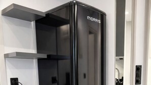 Uma geladeira preta com a marca 'Morris' na porta, uma bancada branca e um design de cozinha moderno.