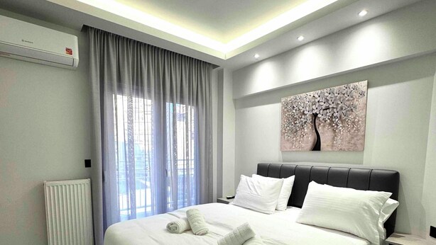 Quarto de hotel moderno com uma cama grande, um radiador, uma janela com cortinas e uma obra de arte na parede.