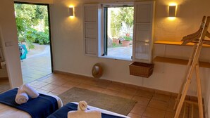 Quarto com duas camas, janela com persianas, prateleira na parede, escada de madeira e vista para o jardim.