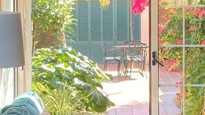 Quarto com sofá, mesa e cadeira, porta de vidro deslizante que dá para área externa com vegetação e um alpendre.