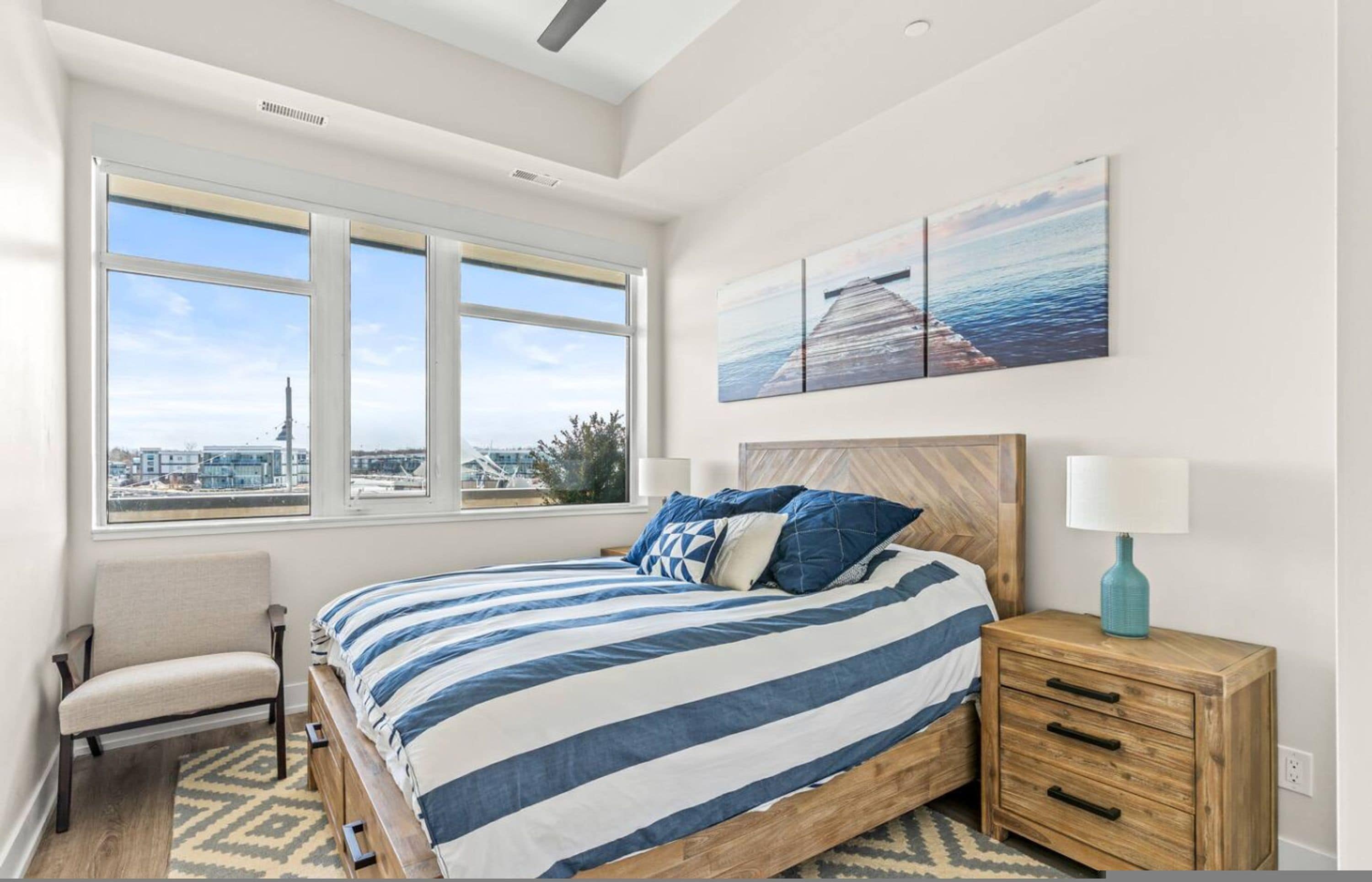 A bedroom with a large bed, a chair, a nightstand, and a view of the city through large windows.