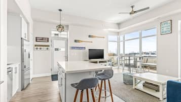 A modern kitchen with a central island, bar stools, a TV, and a dining area with a view.