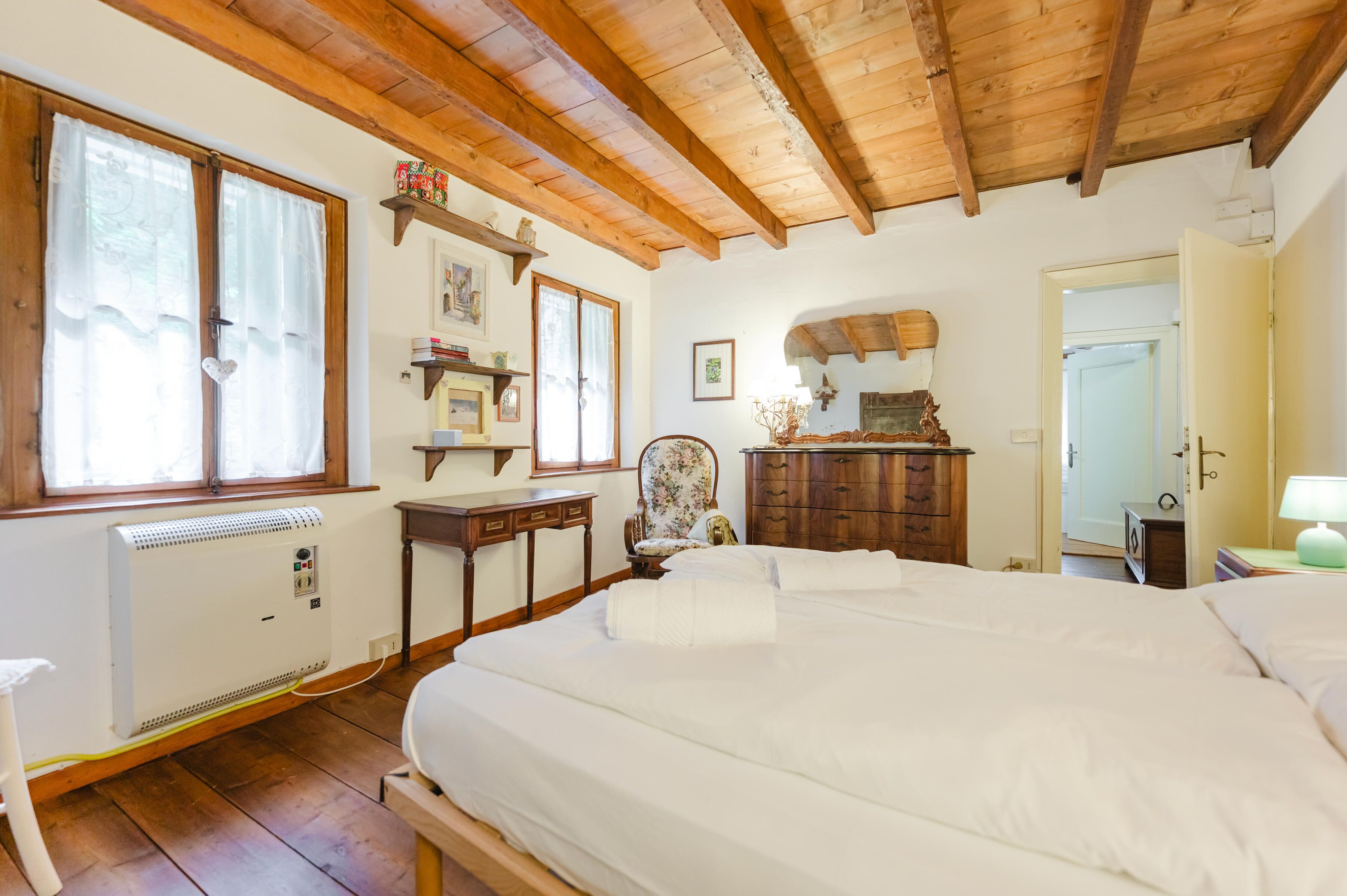 Una camera da letto con soffitto in legno, un letto con lenzuola bianche, un termosifone, una scrivania e una sedia.