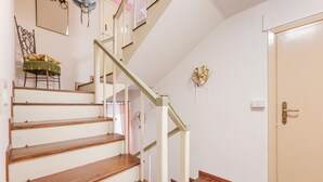 Un escalier avec des marches en bois et une rampe blanche, une chaise recouverte d’un tissu vert, une porte et un objet décoratif fixé au mur.