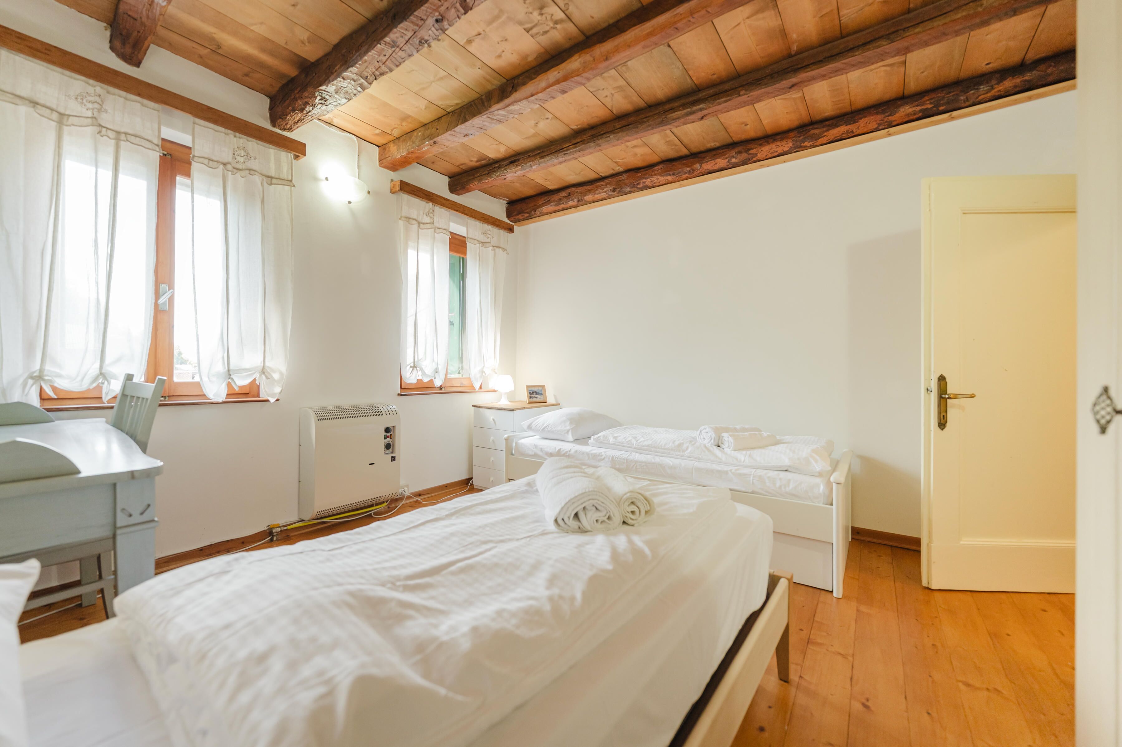 Una habitación con techo de madera, dos camas, un escritorio y un radiador.