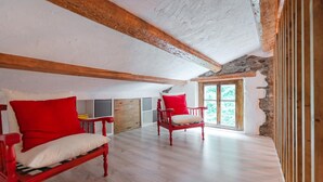 Une pièce avec des poutres en bois, un mur en pierre, une fenêtre et deux chaises rouges dotées de coussins blancs.
