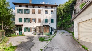 Un immeuble à plusieurs étages, avec une entrée centrale, un portail de garage sur le côté droit et une rue étroite qui y mène.