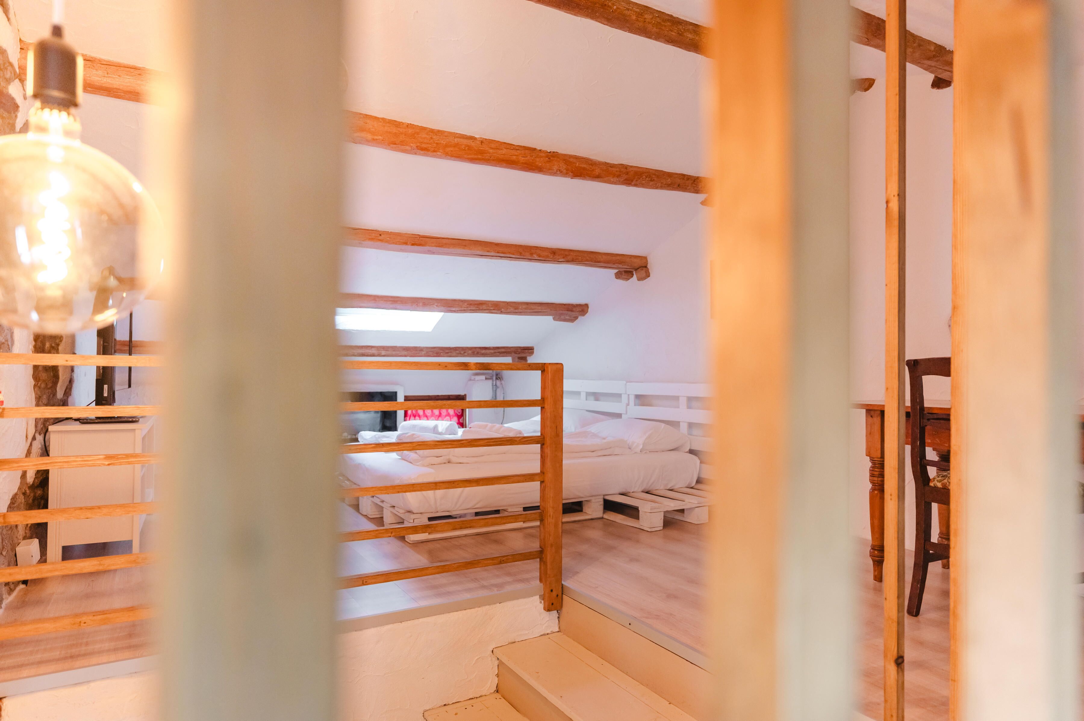 Una habitación con literas, vigas de madera, un escritorio y una lámpara colgante.