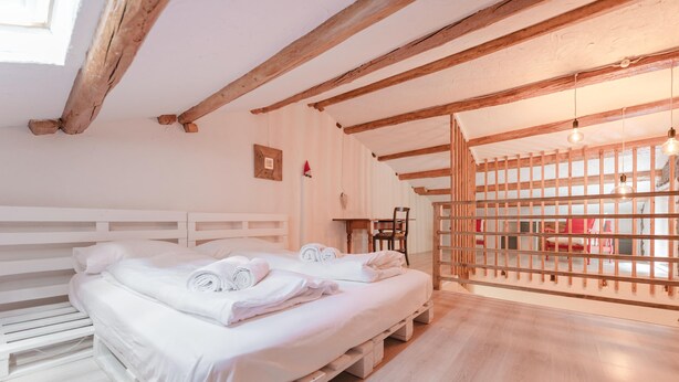 Une chambre avec deux lits, des poutres apparentes, une cloison en bois et un luminaire suspendu.