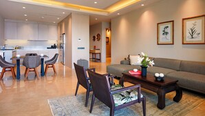 Una sala de estar moderna con un sofá, una mesa de centro y sillas. Se observa una cocina al fondo con armarios y una zona de comedor.
