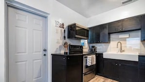 A compact kitchen with a microwave, stove, and sink, wooden flooring, and dark cabinetry. - Cozy house in the heart Of Miami (Miami)