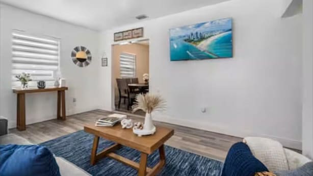 A modern living room with a wooden coffee table, a painting of a beach, and a dining area in the background. - Cozy house in the heart Of Miami (Miami)