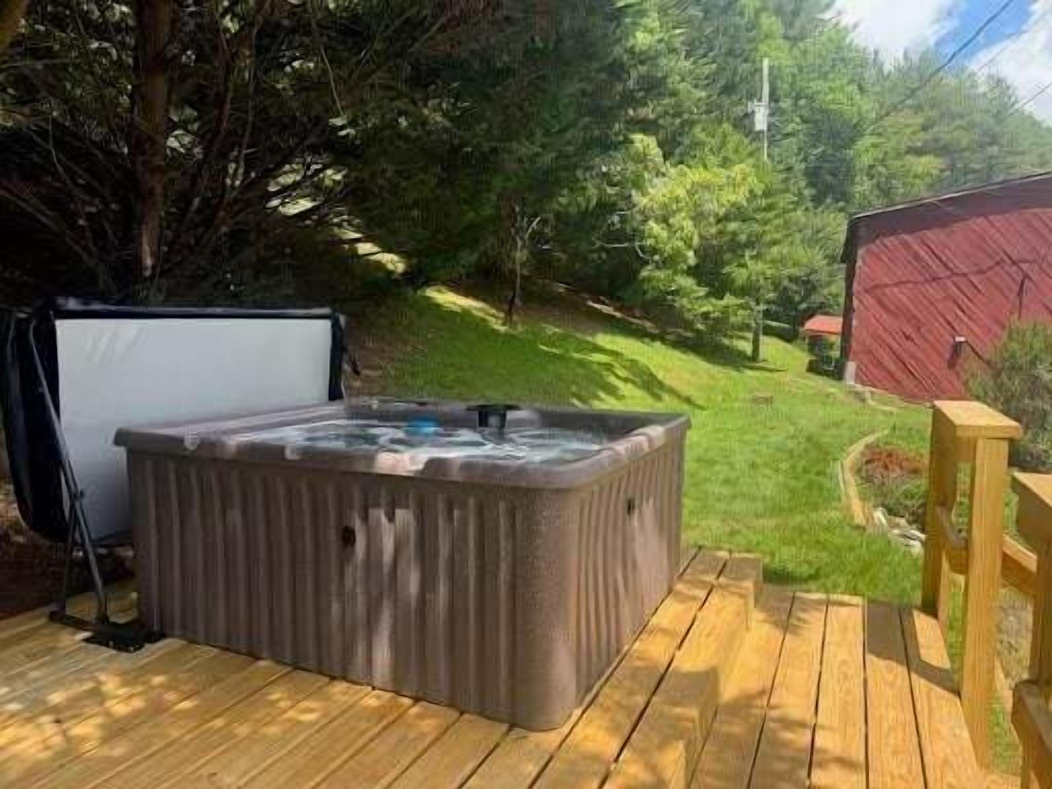 A hot tub on a wooden deck with a grassy yard and a red barn in the background.