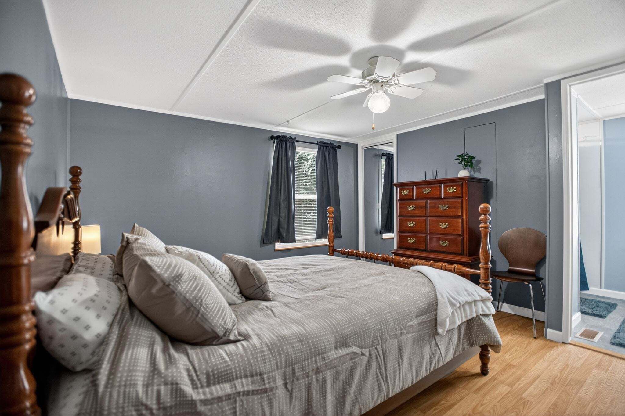 A bedroom with a bed, dresser, chair, and a ceiling fan.
