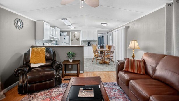 A living room with a brown leather sofa, a brown leather armchair, a wooden coffee table, a patterned rug, a ceiling fan, and a kitchen in the background. - Peaceful Pines - 2br Getaway Near Blue Ridge 2 Bedroom Home (Burnsville)