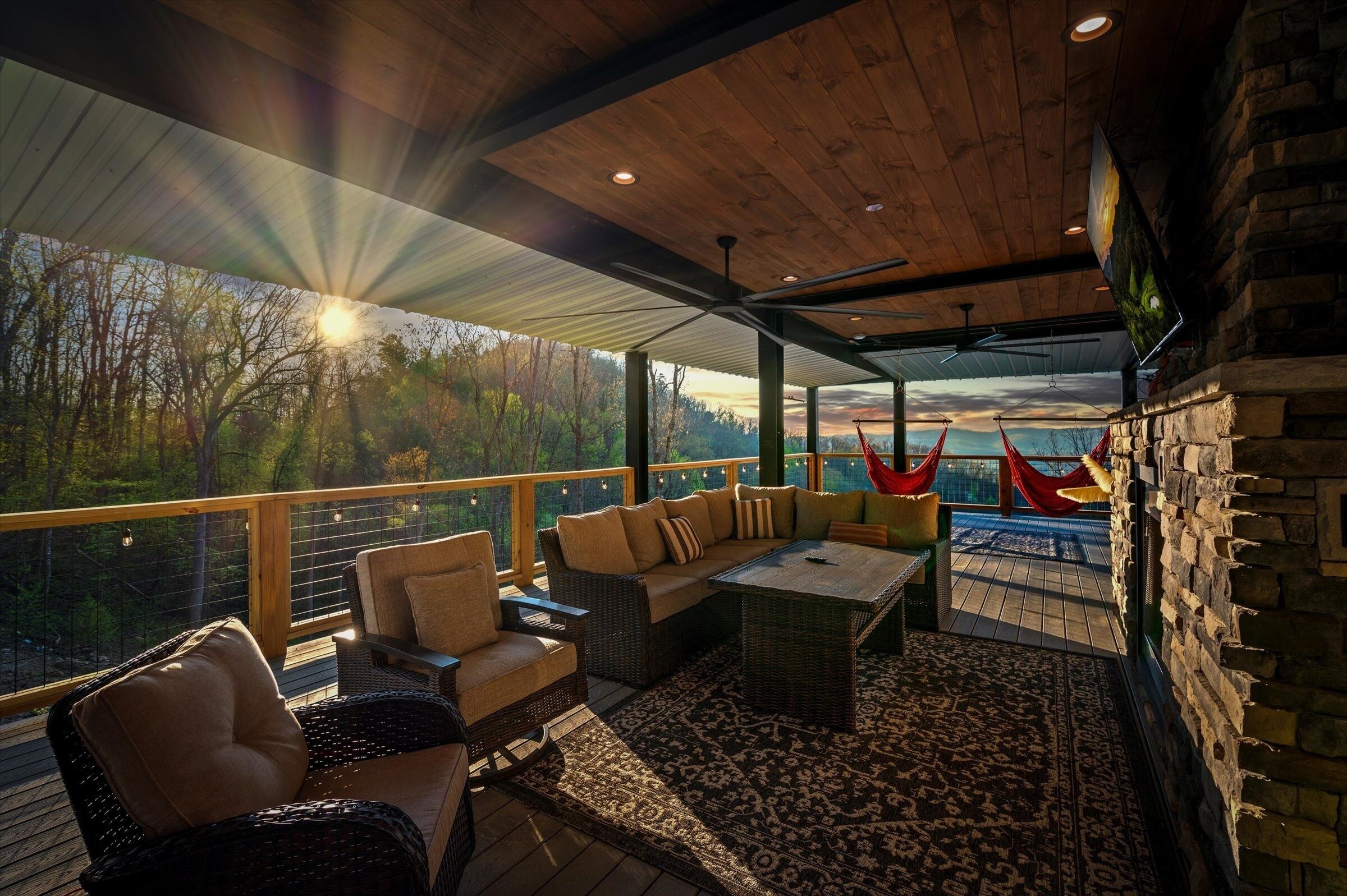 A wooden deck with wicker furniture, a stone wall, and a view of trees.