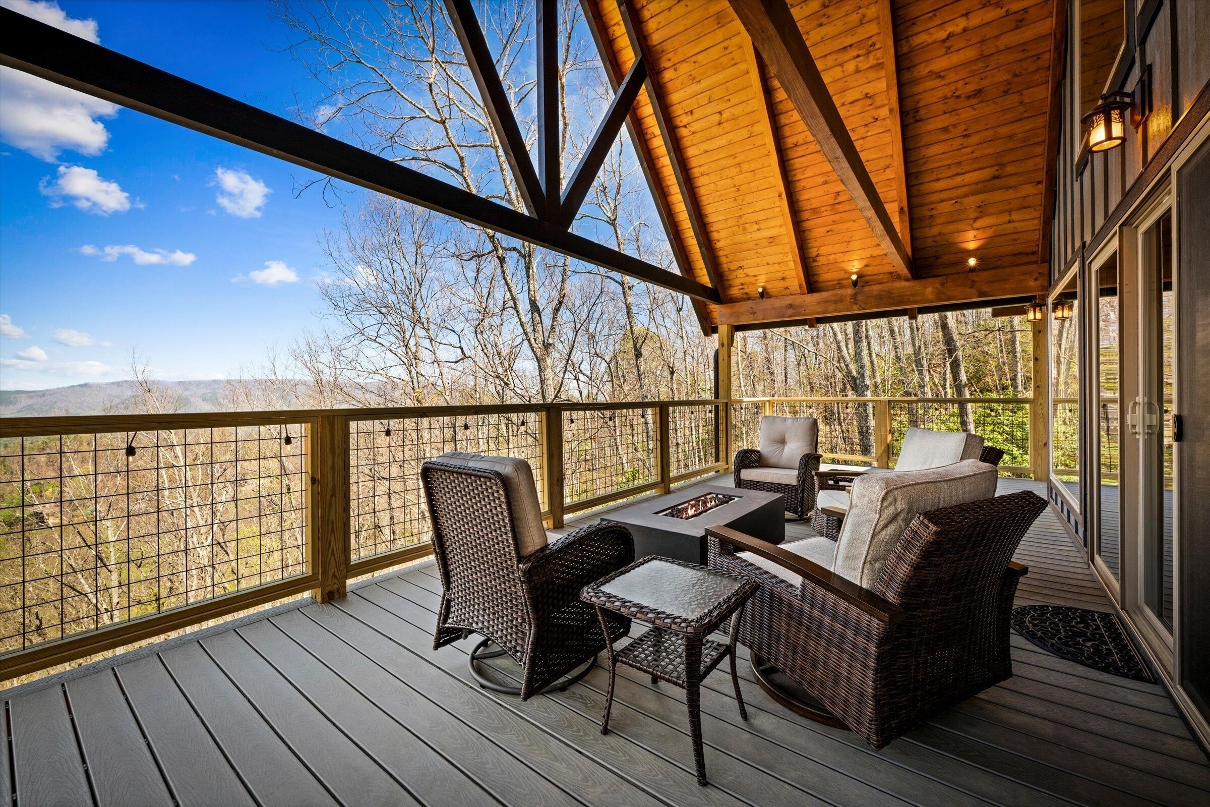 Um terraço coberto ao ar livre com móveis de vime, uma lareira e vista para a paisagem circundante.