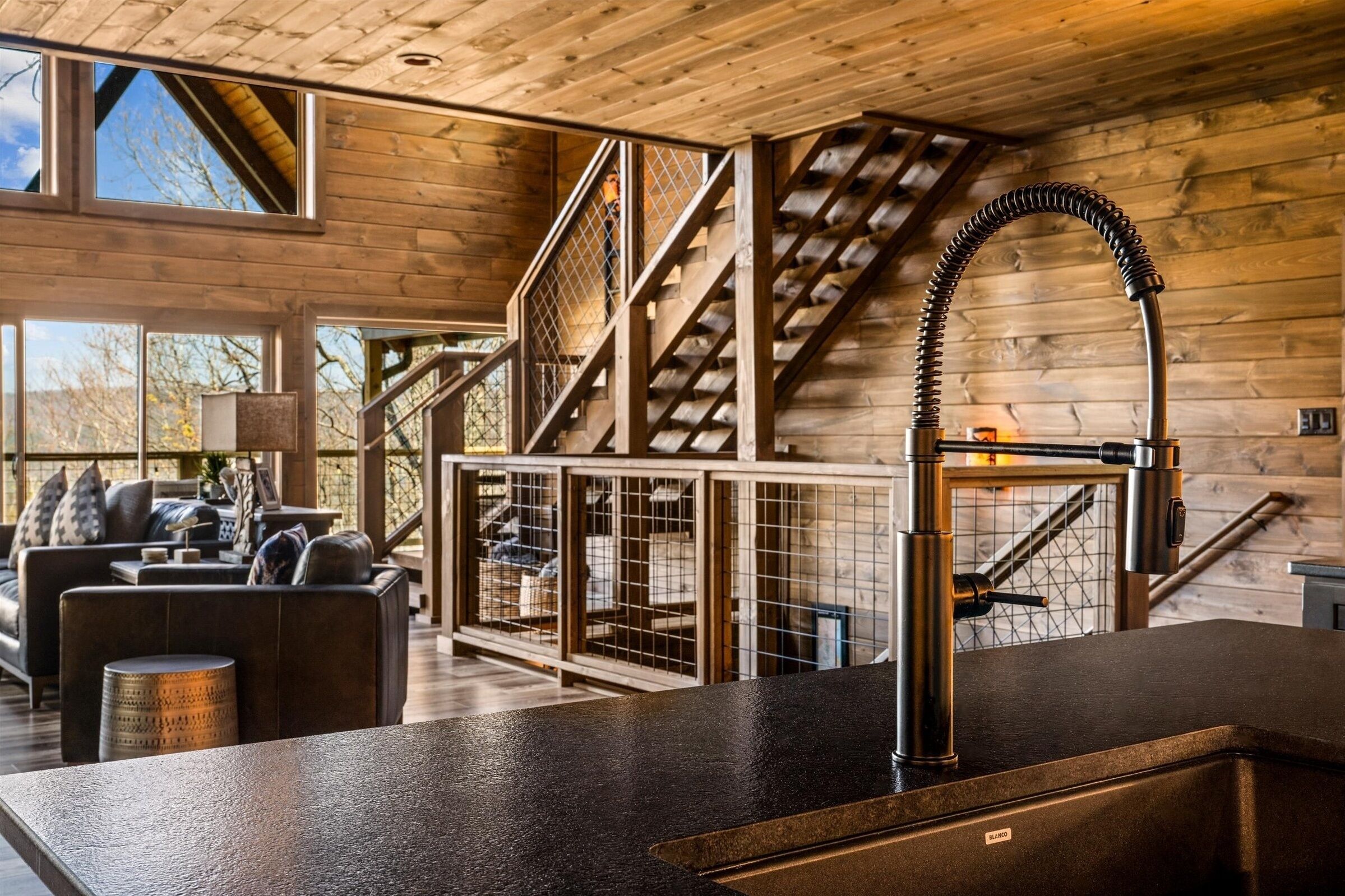 A modern interior with a kitchen area, wooden walls, a staircase, and a seating area with a sofa and coffee table.