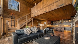 A spacious living area with a wooden staircase, a sofa with cushions, a coffee table, and a kitchen with stone countertops. - Kelly's Escape Cabin (Sevierville)