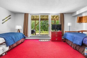 Ein Hotelzimmer mit zwei Betten, einem Fernseher, einem Schminktisch und einer Glastür zum Balkon.