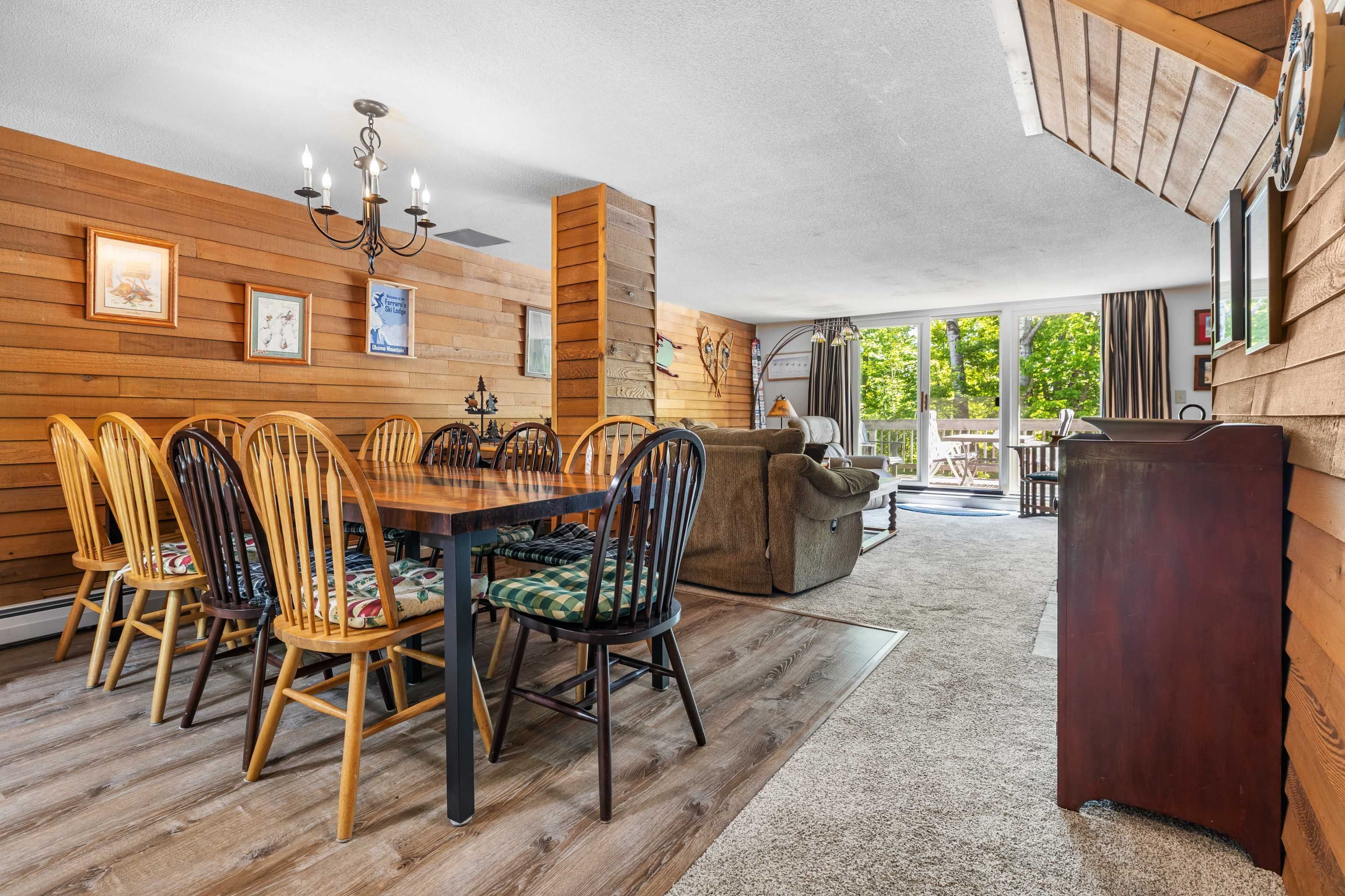 A dining area with a wooden table and chairs, a chandelier, and a view of the outdoors.