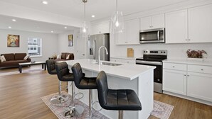 A modern kitchen with white cabinets, stainless steel appliances, and a central island with bar stools. - New 4br Townhome Near Harpers Ferry 4 Bedroom Townhouse (Charles Town)