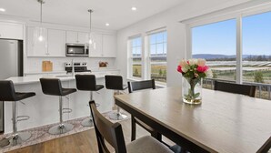 A modern kitchen with white cabinets, stainless steel appliances, and a dining area with a wooden table and black chairs. - New 4br Townhome Near Harpers Ferry 4 Bedroom Townhouse (Charles Town)