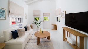 A modern living room with a sofa, coffee table, TV stand, and a large window. - Haynes House 5 Bedroom Home (Holetown)