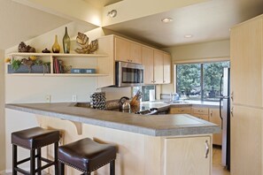 A kitchen with a large island, wooden cabinets, a microwave, and a refrigerator. - River Ridge 429a 2 Bedroom Condo (Bend)