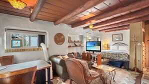 A cozy room with a wooden ceiling, a desk with chairs, a sofa, a television, and a bed with a patterned bedspread. - Casita Adobe Duplex (Grand Junction)