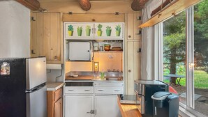 A compact kitchen with wooden cabinets, a built-in oven, a sink, and a window overlooking greenery. - Casita Adobe Duplex (Grand Junction)