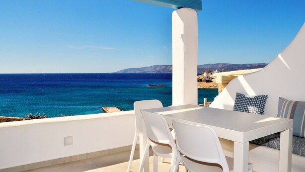A terrace with a table and chairs, overlooking a clear blue sea and distant mountains.