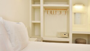 A hotel room with a bed, a wardrobe with hanging clothes, a small table, and a mirror. - Villa Amorgos, Sohoro Koufonisia (Koufonisia)