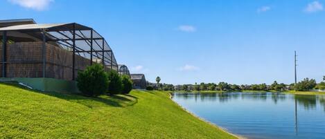 A modern building with a glass structure, a grassy area, and a calm water body.