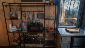 Cocina compacta con microondas, cafetera y varios utensilios en estantes.