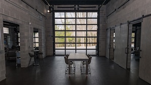 Una habitación amplia con un gran ventanal, una mesa con sillas y una puerta.
