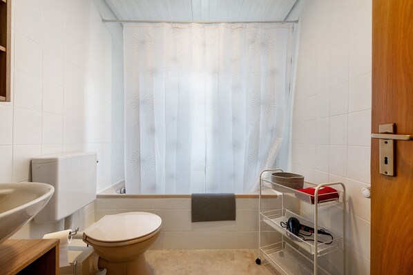 Et badeværelse med toilet, vask, bruseforhæng og en metalkurvhylde.