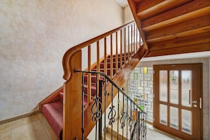 Una escalera de madera con un rellano alfombrado en rojo, una barandilla de metal y una puerta de vidrio con un símbolo de corazón.