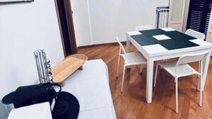 Huoneessa on valkoinen sohva, pieni pöytä, valkoinen ruokapöytä tuoleineen, seinäkello ja patteri.
