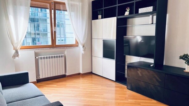 Moderni olohuone, jossa on sohva, seinään integroitu viihdekeskus ja ikkuna, jossa on verhot.