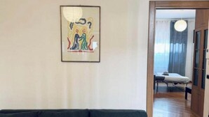 Huoneessa on tummanvihreä sohva, kehystetty abstrakti maalaus ja puulattia.