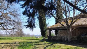 Un edificio de piedra con tejado de tejas, rodeado de césped y árboles.