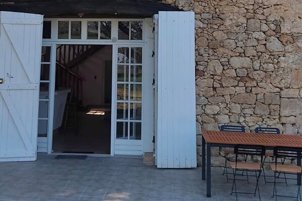 Un muro de piedra, una mesa de madera con sillas y una puerta blanca que da a una escalera.