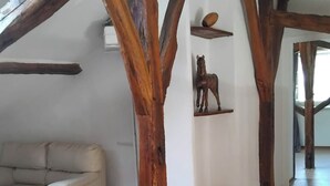 Una habitación con vigas de madera a la vista, un sofá color beige, un taburete de madera y una escultura de caballo sobre una estantería.