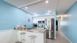 Uma cozinha com ilha central, banquetas, geladeira de aço inoxidável e micro-ondas.